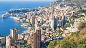 Paesaggio costiero con grattacieli, un porto turistico e montagne sullo sfondo.