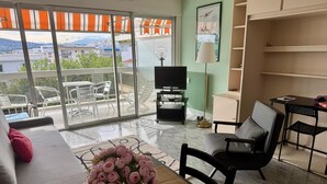 A modern living room with a sofa, a dining table with a vase of flowers, a TV, and a balcony with outdoor furniture.