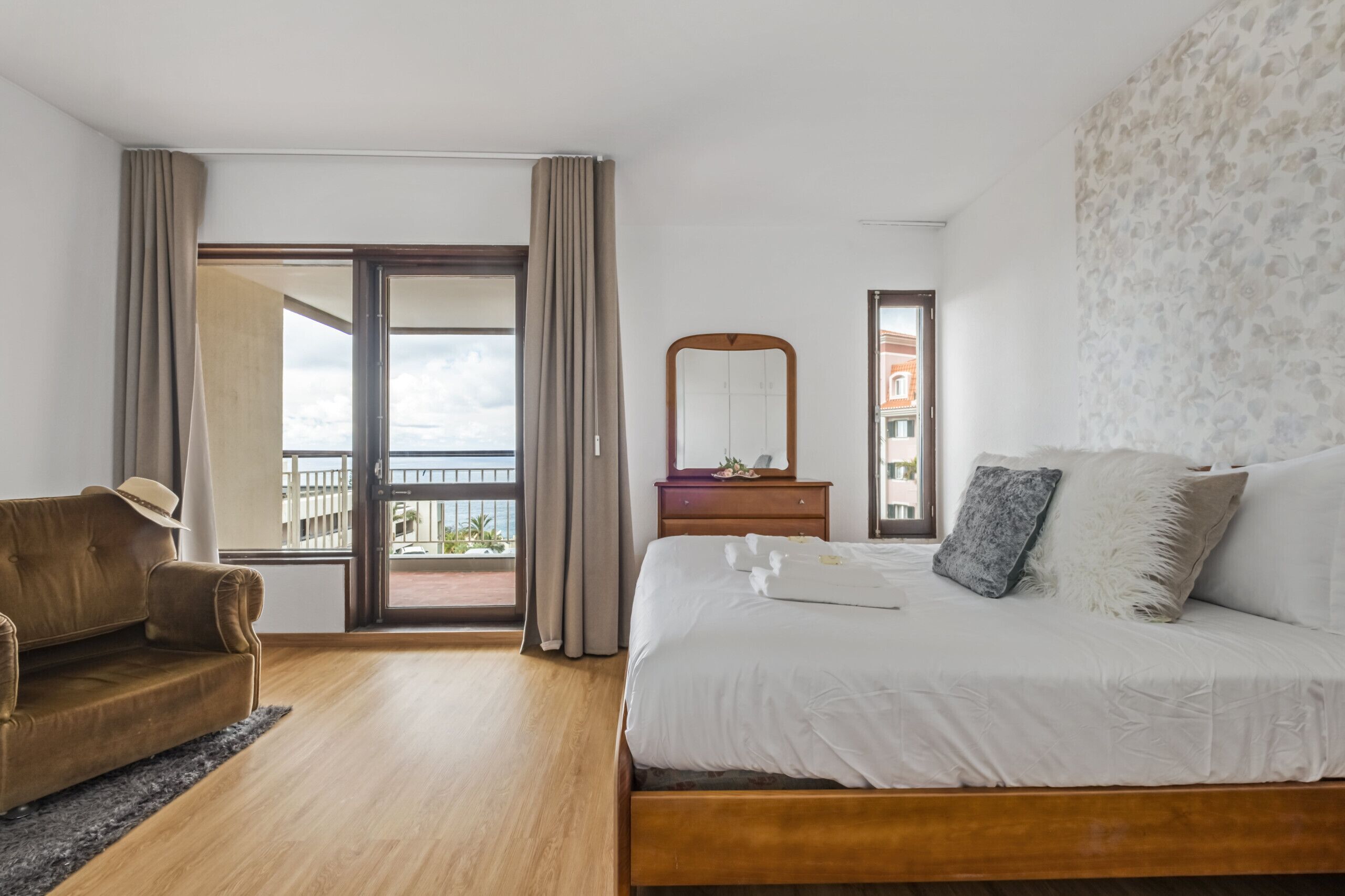 A hotel room with a large bed, a wooden nightstand, a mirror, and a view of the outside balcony.