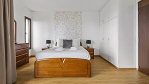 A bedroom with a wooden bed, two bedside tables with lamps, a wardrobe, and a large mirror. - Summertime Stay by Homie (Funchal)