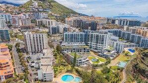 A high-rise residential building complex with multiple balconies, a central courtyard with a swimming pool, and a view of the coastline. - Summertime Stay by Homie (Funchal)