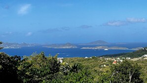 Un paysage côtier offrant une vue sur la mer, des îles lointaines et une zone vallonnée parsemée de végétation et de bâtiments.