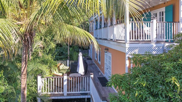 Un immeuble à plusieurs étages doté d’un balcon, entouré d’une végétation luxuriante et de palmiers.