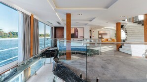 Un interior espacioso con balaustrada de cristal con vistas a una extensión de agua, una escalera curva y una sala de estar moderna con sofá y mesa de centro.