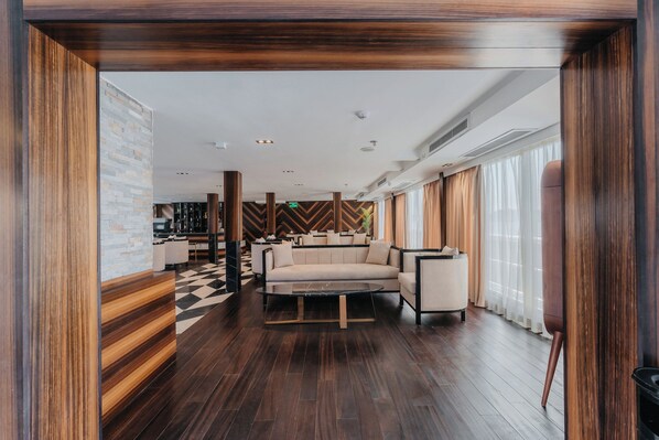 A modern hotel lobby with a central seating area, wooden flooring, and a checkered floor pattern.