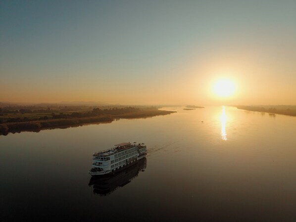 Un bateau à vapeur navigue sur une rivière paisible, avec un lever de soleil en arrière-plan.