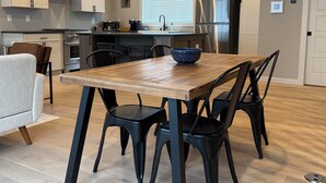 A modern kitchen with white cabinets, a stainless steel refrigerator, and a wooden dining table with black chairs.