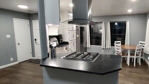 A modern kitchen with a central island, white cabinetry, and a dining area with a table and chairs. - Entire home just 14 miles from Lassen Volcanic National Park (Shingletown)
