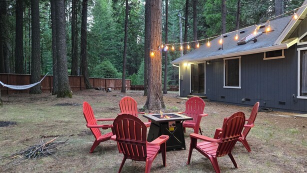 A wooden deck with Adirondack chairs and a fire pit, surrounded by tall trees. - Entire home just 14 miles from Lassen Volcanic National Park (Shingletown)