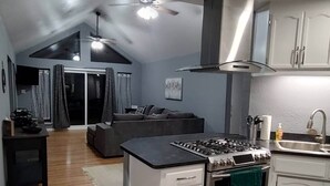 A compact kitchen with a gas stove, a sink, and a small countertop. There is a sliding glass door leading to a living area with a sofa and a ceiling fan. - Entire home just 14 miles from Lassen Volcanic National Park (Shingletown)