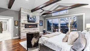 Un dormitorio con chimenea, una cama grande, vistas al exterior y un ventilador de techo.