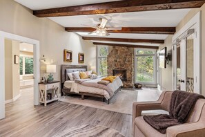 Relax in this serene bedroom with a large bed, stone fireplace, and expansive window offering a view of the outdoors.