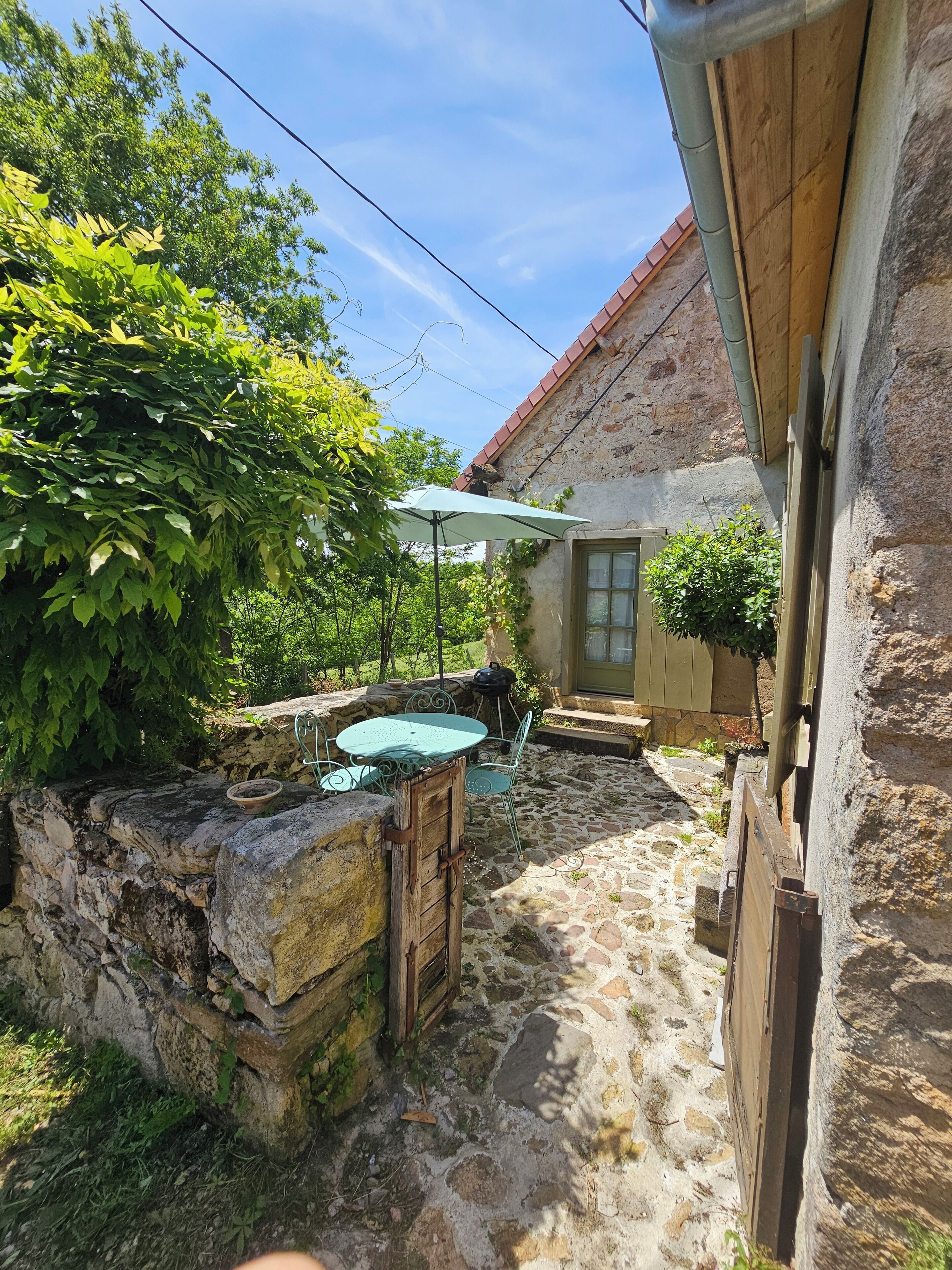 Eine Steinterrasse mit Tisch und Stühlen, eine Holztür und ein kleiner Garten mit einem Blumentopf.