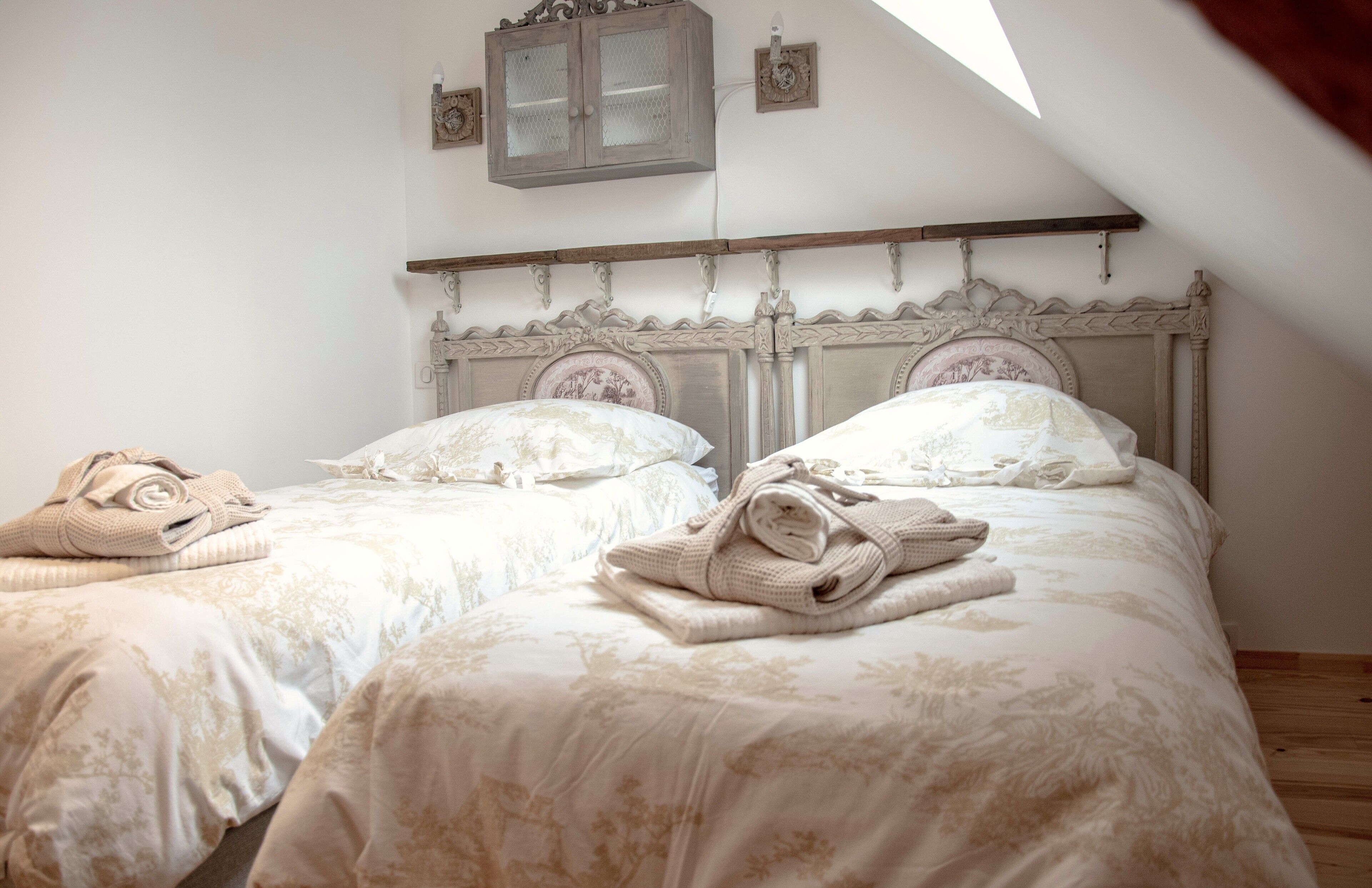 A bedroom with two beds, each with a wooden headboard and floral bedding. There are towels on each bed, and a small cabinet above the beds.