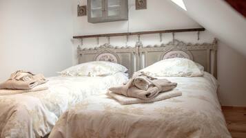 A bedroom with two beds, each with a wooden headboard and floral bedding. There are towels on each bed, and a small cabinet above the beds.