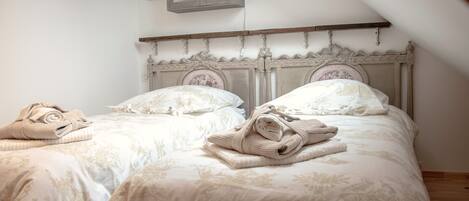 A bedroom with two beds, each with a wooden headboard and floral bedding. There are towels on each bed, and a small cabinet above the beds.