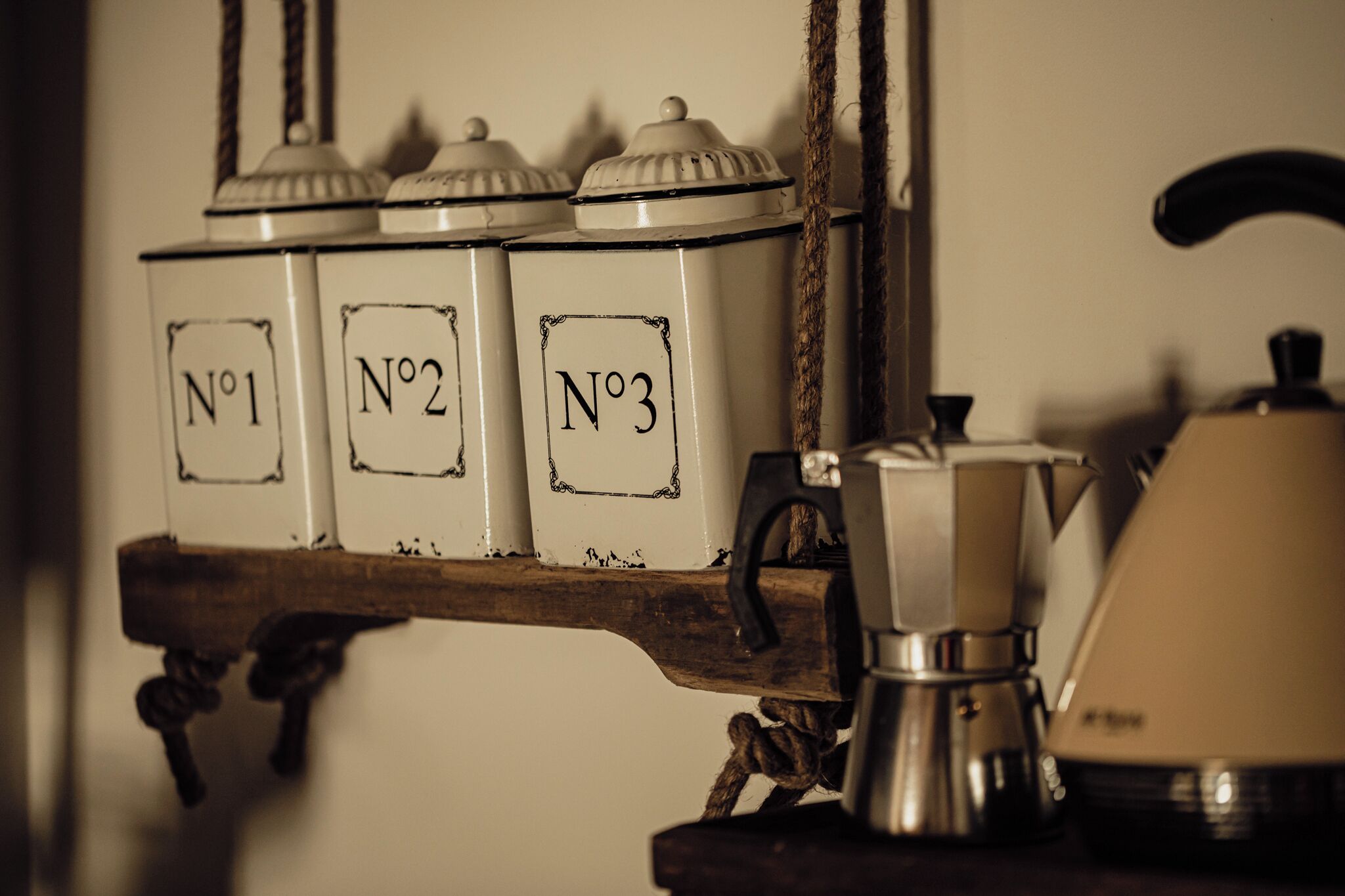 Une cuisine avec trois récipients étiquetés (n° 1, n° 2, n° 3) placés sur une étagère en bois, une machine à café et une casserole suspendue.
