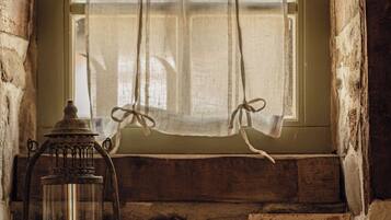 A rustic window with a curtain, a lantern, and a framed picture on a stone ledge.