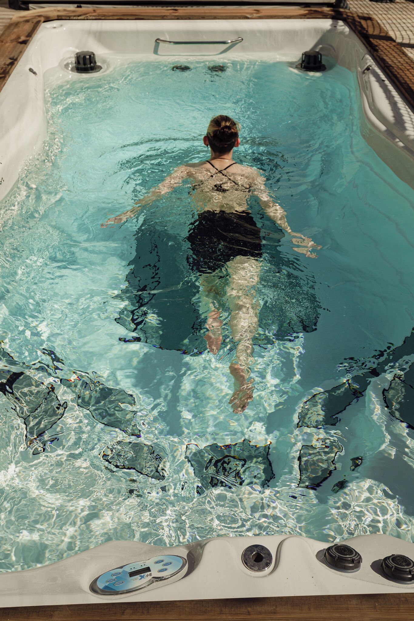 A person swimming in a hot tub with a control panel at the bottom.