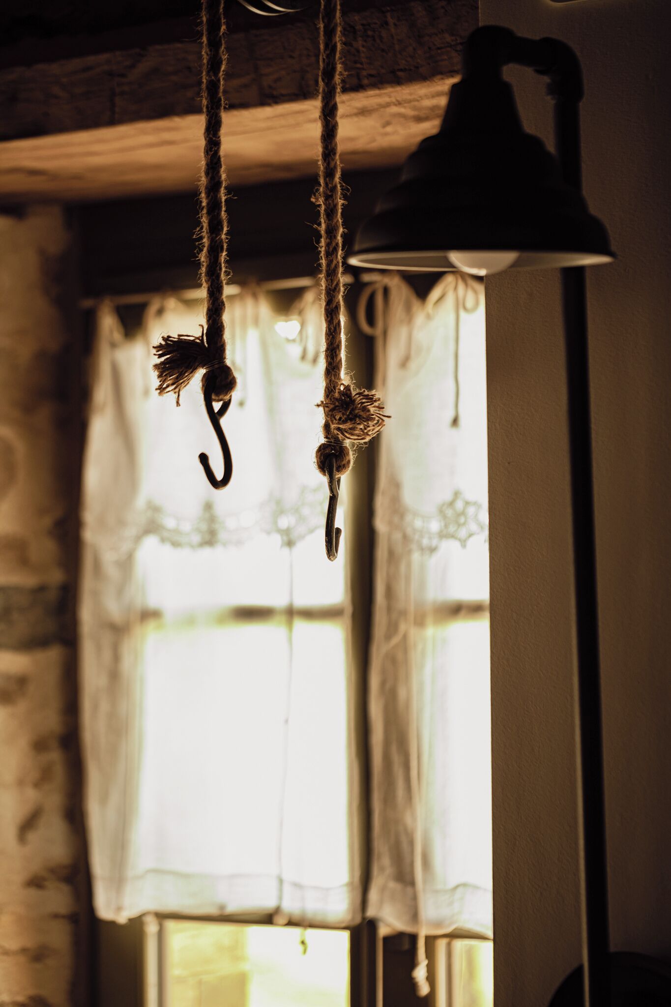A room with a hanging lamp, a hook, and a window with curtains.
