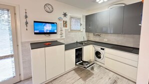 Una cocina compacta con lavadora, un lavabo y un televisor montado en la pared.