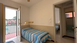 Un dormitorio con cama, ventilador de techo, ventana y puerta que da a otra habitación.