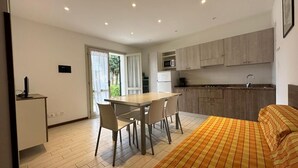 Un dormitorio moderno con cama, una zona de comedor con mesa y sillas, y una cocina con armarios y electrodomésticos.