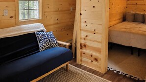 Interior de una cabaña de madera con un sofá, una ventana y una cama.