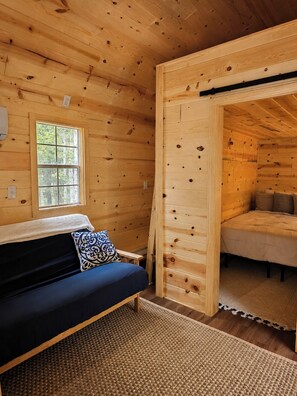 A wooden cabin interior with a sofa, a window, and a bed.