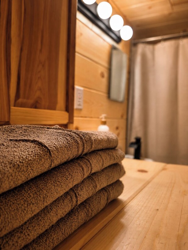 A stack of towels on a wooden table in a room with wooden walls and a curtain. - Cozy Tiny Cabin Near Leech Lake complete with Firepit + Trails (Walker)