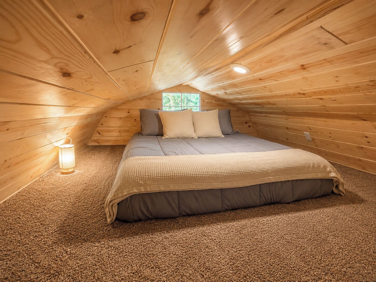 A cozy attic bedroom with a bed, pillows, a lamp, and a window.