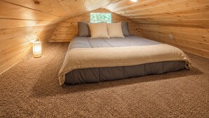 Un dormitorio acogedor en el ático con cama, almohadas, una lámpara y una ventana.