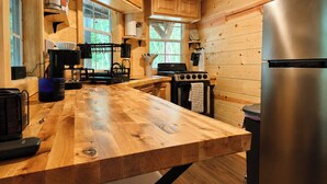 Interior de una cabaña de madera con cocina, que incluye una encimera de madera, estufa, refrigerador y ventana que proporciona luz natural.