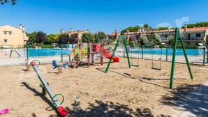 A playground with swings and a slide, a swimming pool, and buildings in the background.