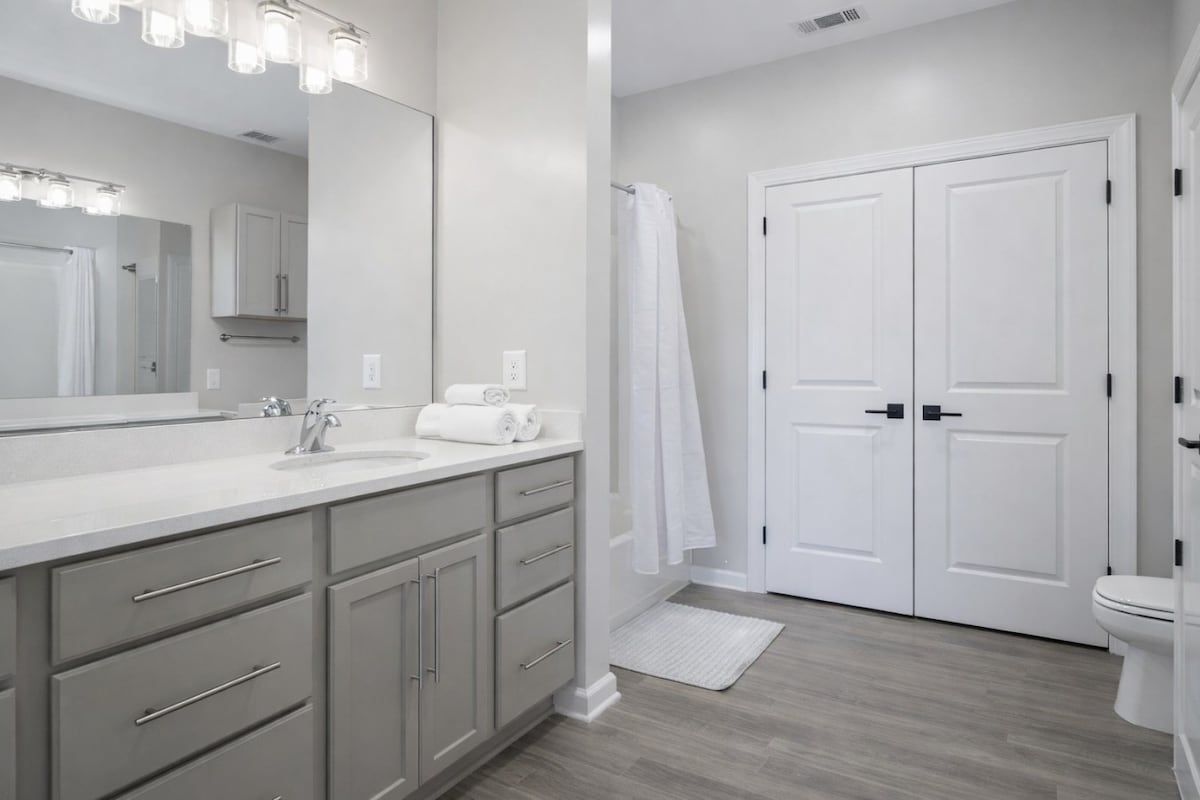 A modern bathroom with a vanity, mirror, and double doors.