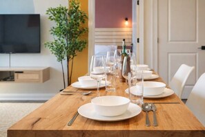 A dining table set with white plates, bowls, and glasses, with a television and a plant in the background.
