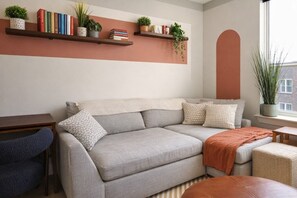 A living room with a sofa, a coffee table, and a bookshelf with books and plants.