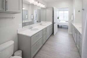 Un baño moderno con tocador doble, un espejo grande y una ducha a ras de suelo.