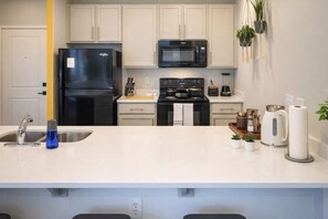 A modern kitchen with a black refrigerator, a microwave, a stove, and a sink. There are potted plants on the counter.