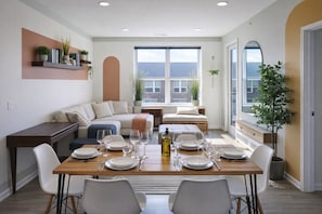 Un comedor moderno con una mesa de madera dispuesta para seis personas, rodeado de sillas blancas.