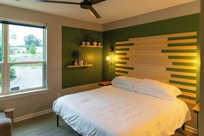 Een slaapkamer met een bed, een plafondventilator, een raam en een wandplank met planten.
