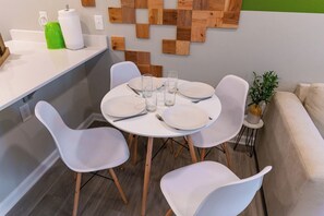 A dining area with a round table set for four, surrounded by white chairs.