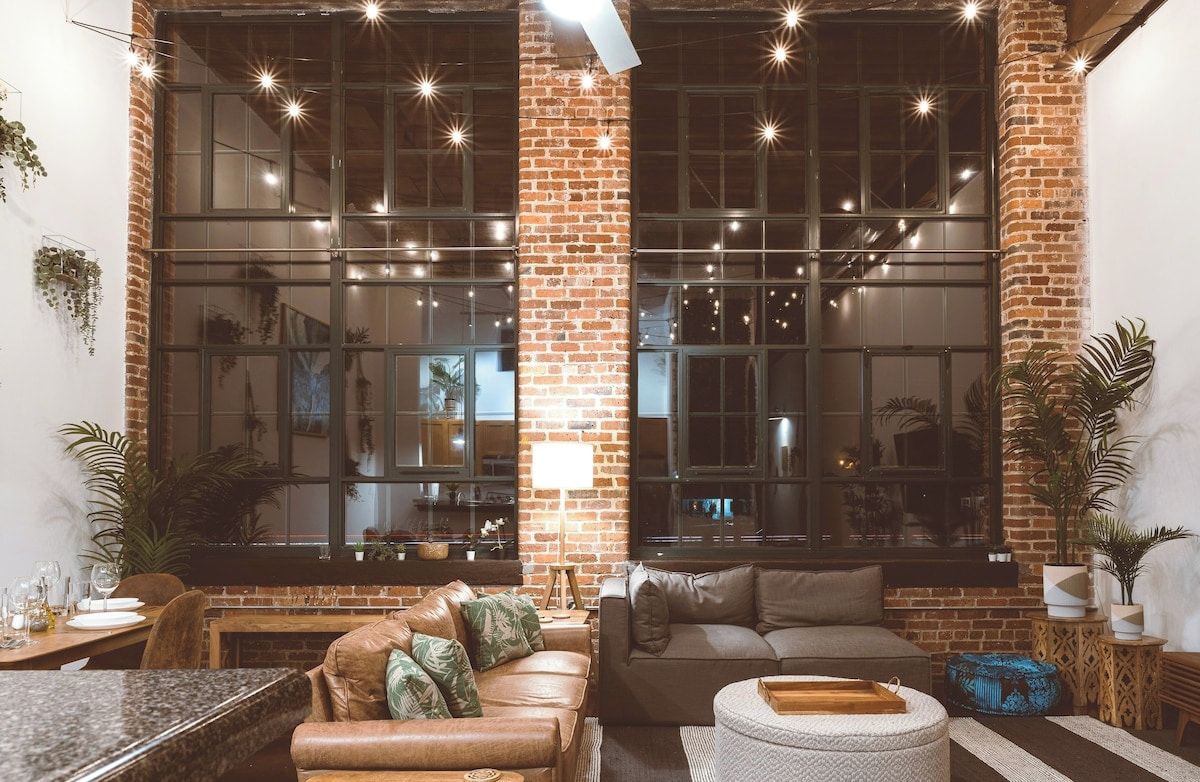 A cozy living area with a brick wall, large windows, and a seating arrangement including a sofa and a coffee table.