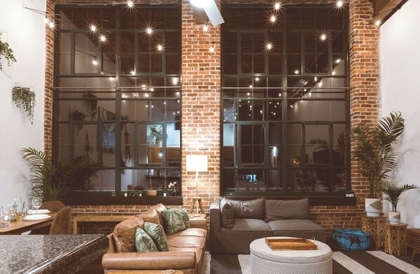 A cozy living area with a brick wall, large windows, and a seating arrangement including a sofa and a coffee table.