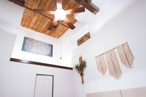 Una habitación con ventilador de techo de madera, una obra de arte enmarcada, tapices de macramé, una puerta y una planta.