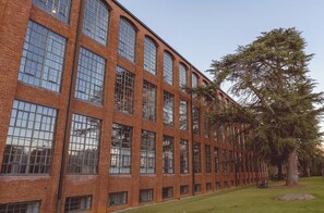 A red brick building with large windows and a tree in the foreground. - Cozy Mill Loft w/ 2 king beds, huge windows (Spartanburg)