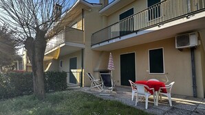 A building with a balcony, outdoor seating, and a tree.