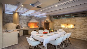 A modern outdoor dining area with a stone wall, a pizza oven, and a built-in grill.