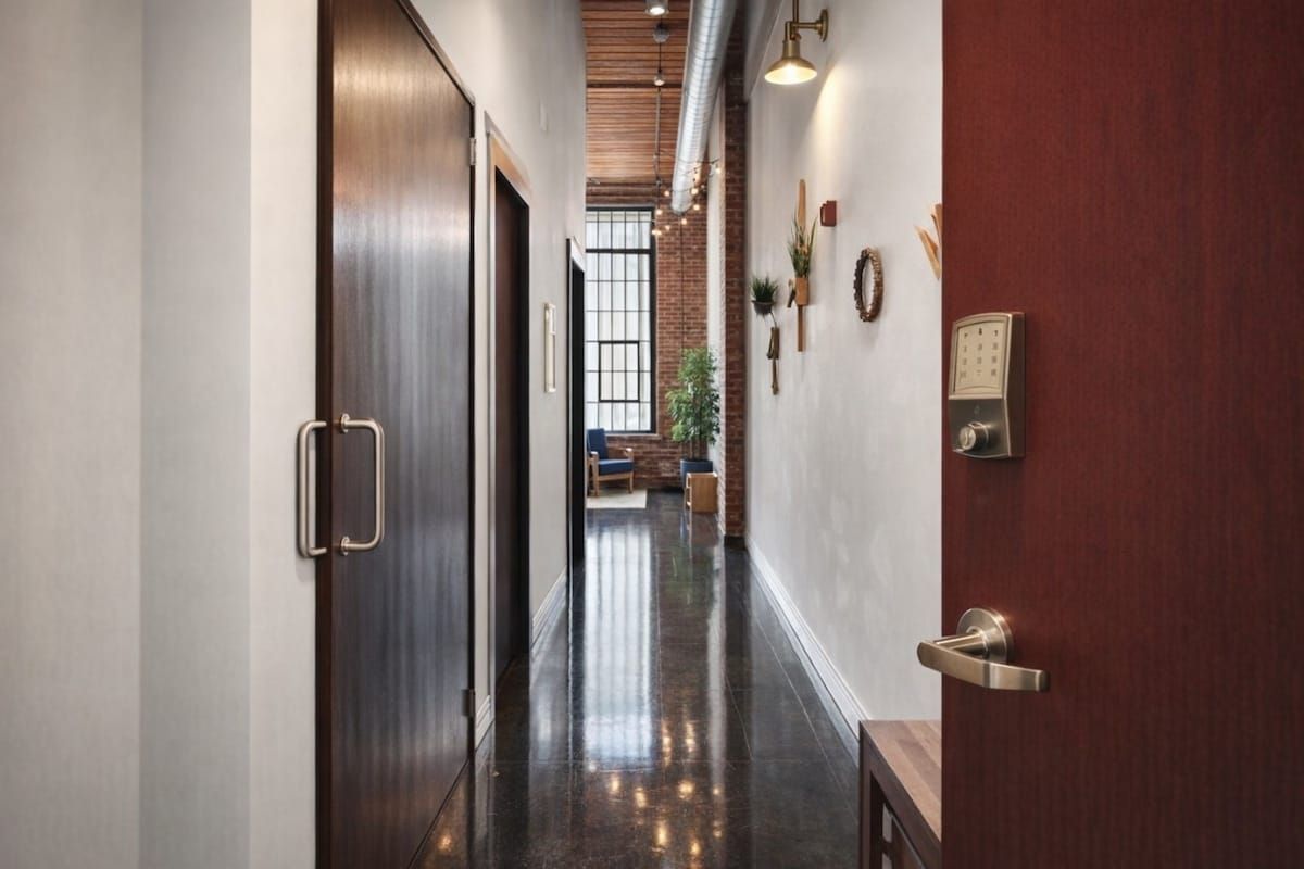 Un couloir avec une porte en bois, un luminaire fixé au mur et un interphone.