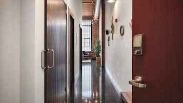 Un couloir avec une porte en bois, un luminaire fixé au mur et un interphone.